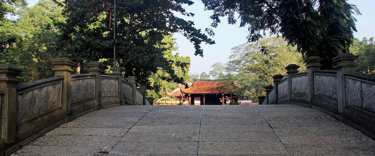 A stone pathway leading to a traditional building with a tiled roof, surrounded by trees.