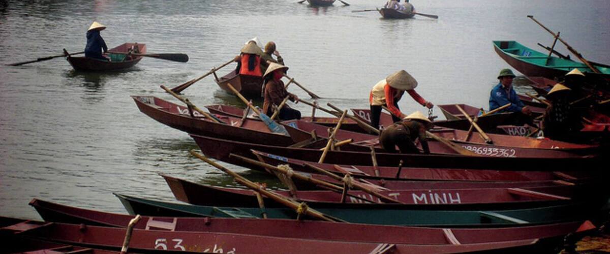 Several traditional boats with people paddling them on a calm river.
