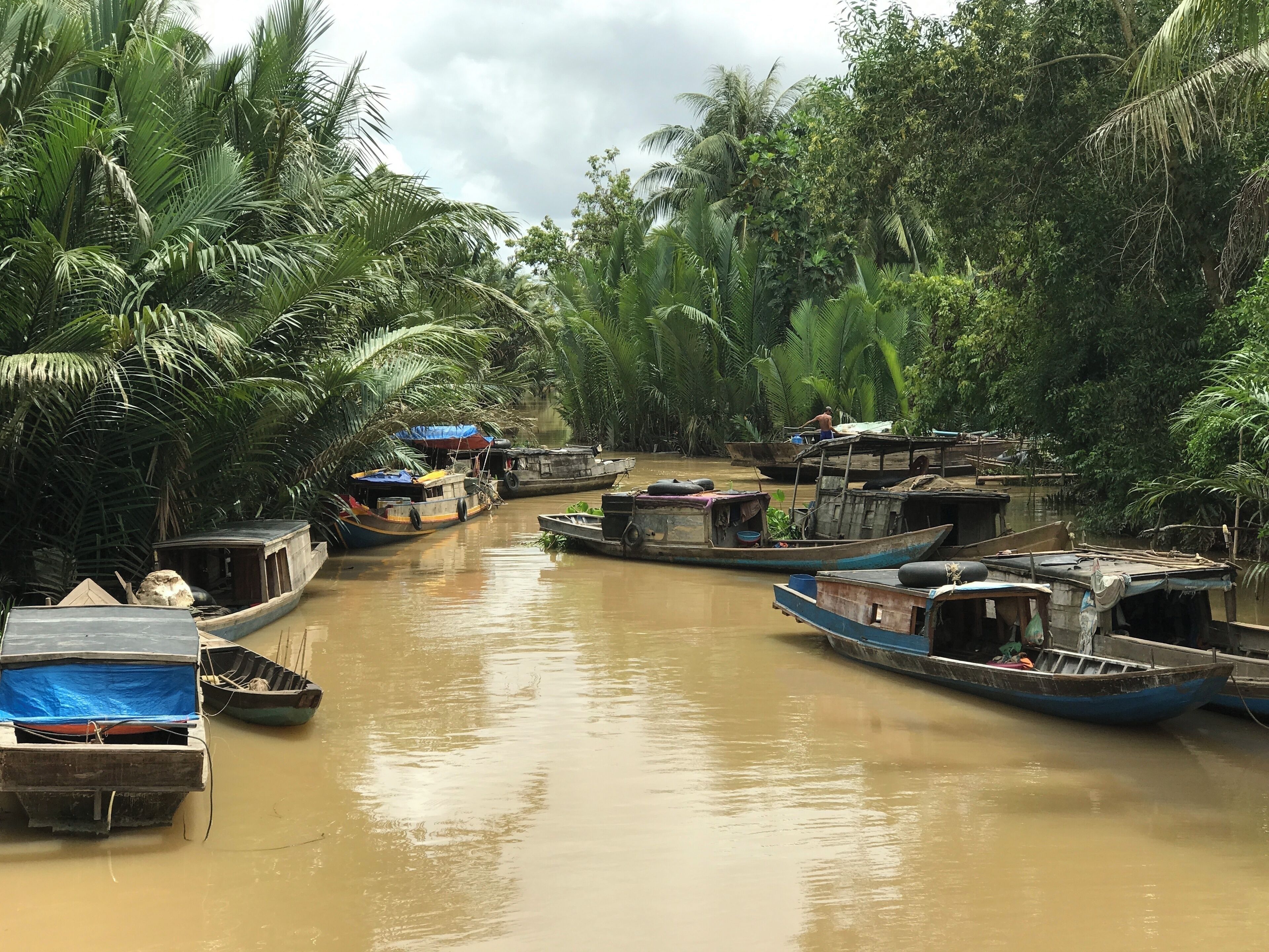 A narrow waterway lined with boats and dense tropical vegetation.