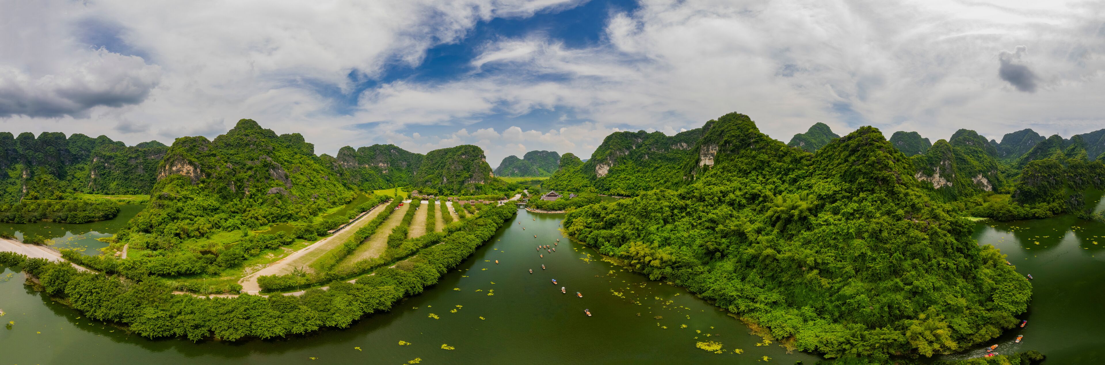 Aerial view of lush mountains, serene river, and tranquil cave in Trang An, Ninh Binh, Vietnam.