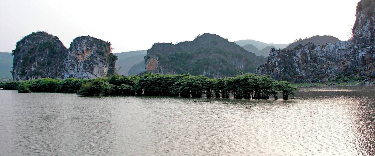 A calm river with rocky cliffs and a cluster of trees in the foreground.