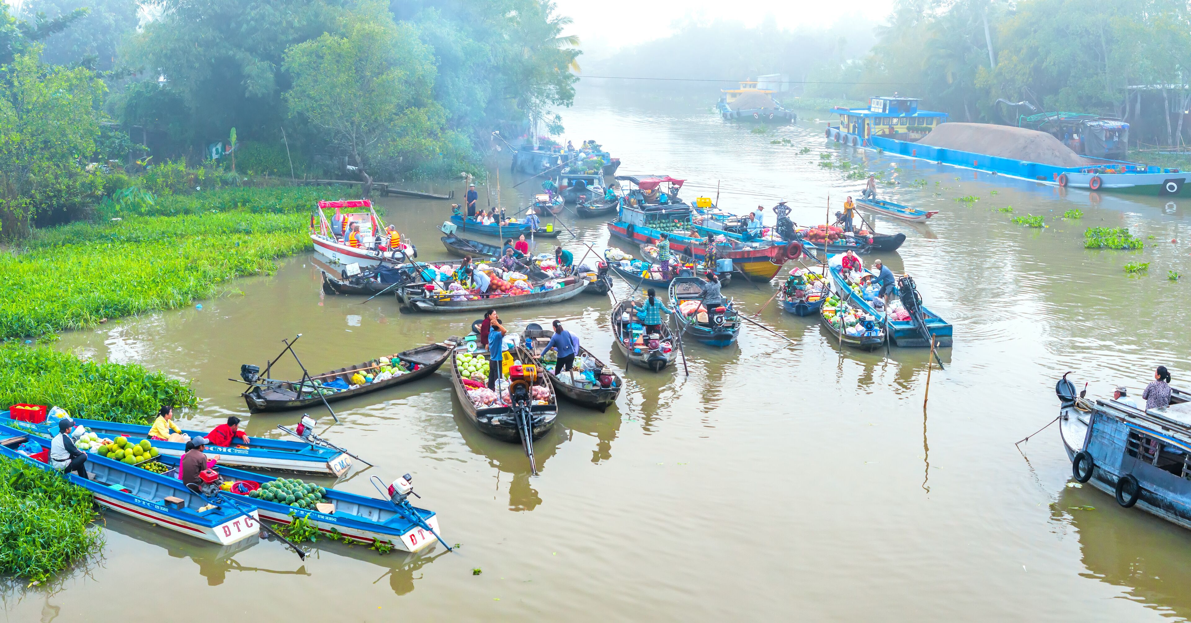 A river with numerous boats docked along the banks, surrounded by lush greenery.