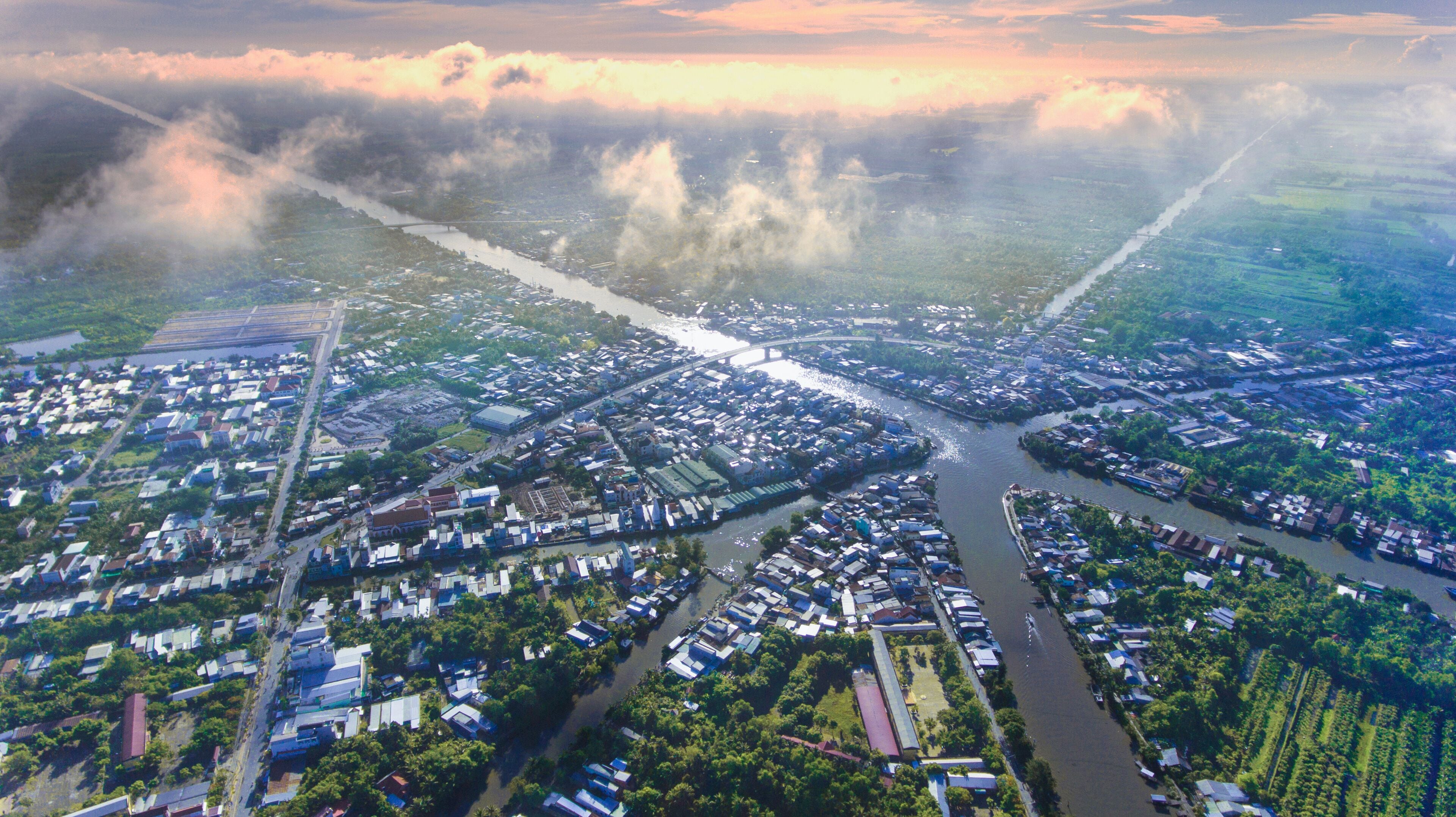 An aerial view of a city with a river running through it, surrounded by greenery and industrial areas.