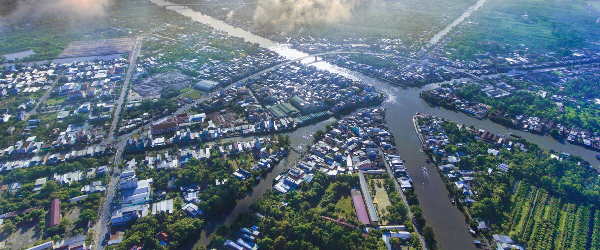 An aerial view of a city with a river running through it, surrounded by greenery and industrial areas.