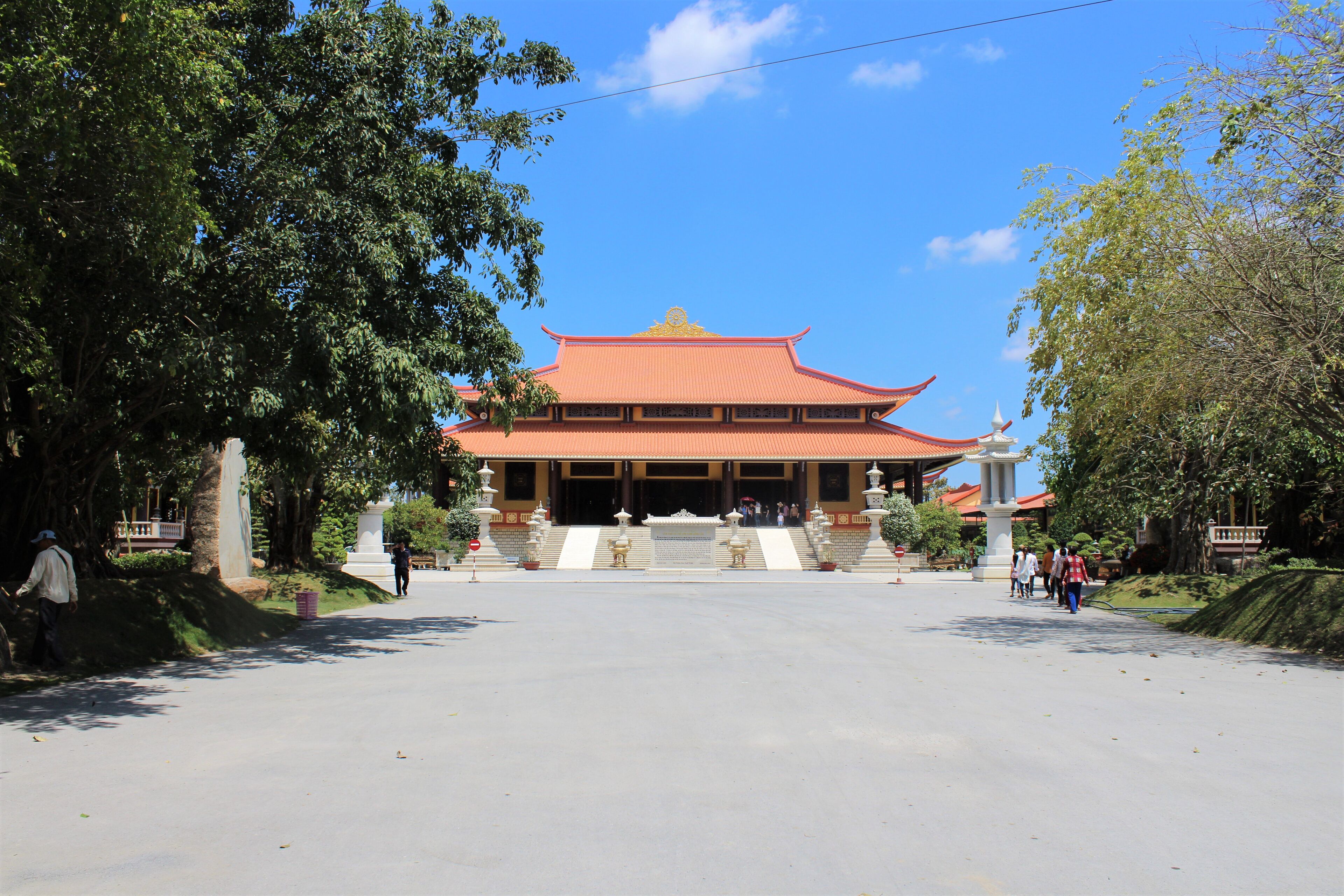 A traditional building with a red roof and golden accents, surrounded by trees and a clear blue sky.