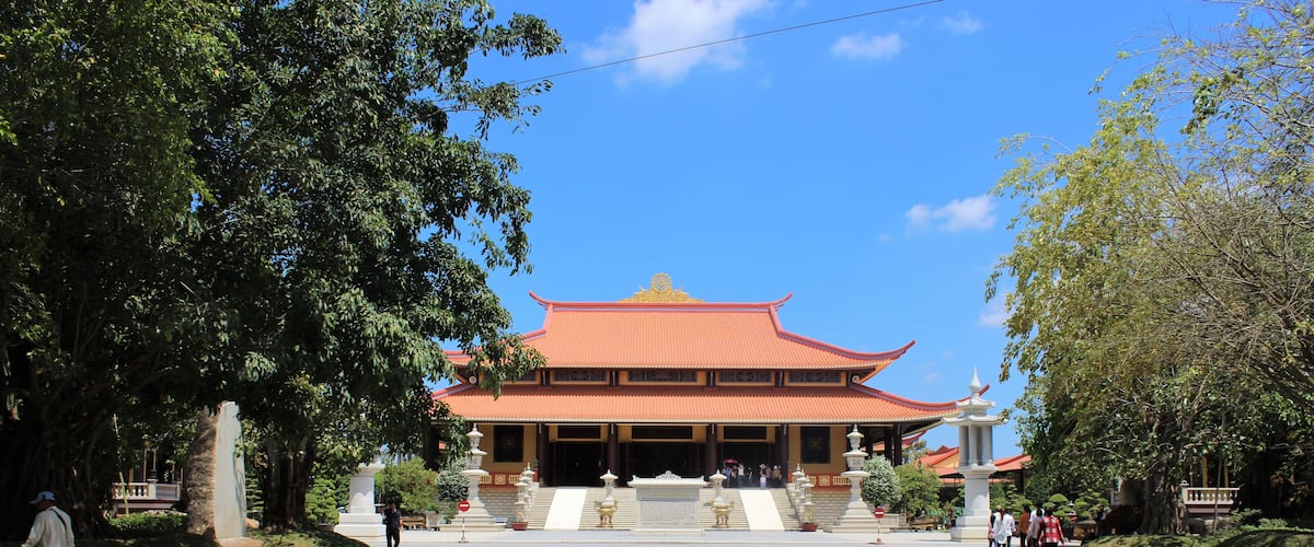 A traditional building with a red roof and golden accents, surrounded by trees and a clear blue sky.