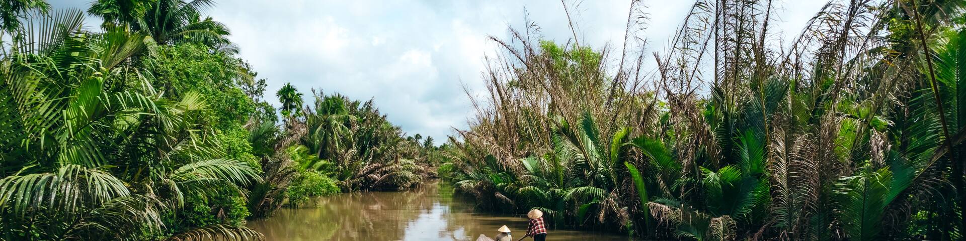 tourist on sampan boat cruise in the Mekong river canals with woman paddling in Vietnamese hat
