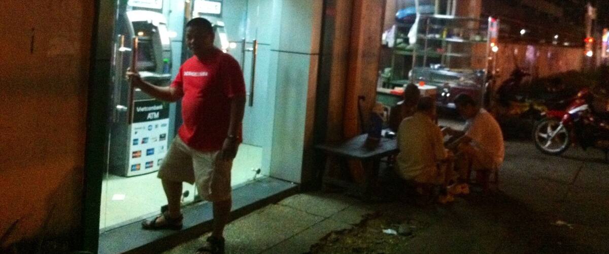 A night scene outside a Vietcombank ATM with people sitting nearby.