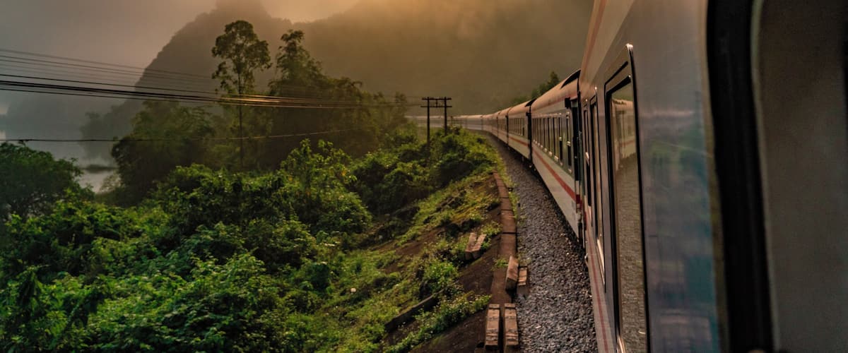 A train traveling through a mountainous landscape with lush greenery and a misty atmosphere.