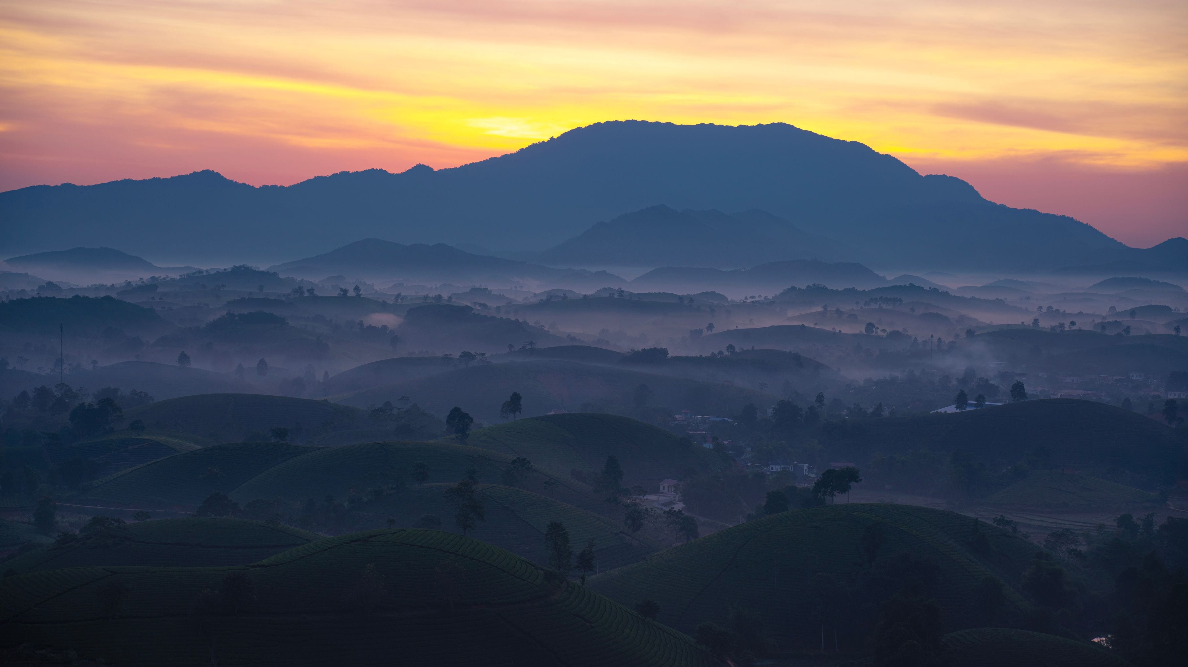 Un paisaje montañoso con colinas ondulantes y un amanecer o atardecer.