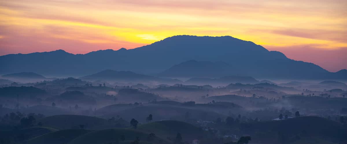 A mountainous landscape with rolling hills and a sunrise or sunset.