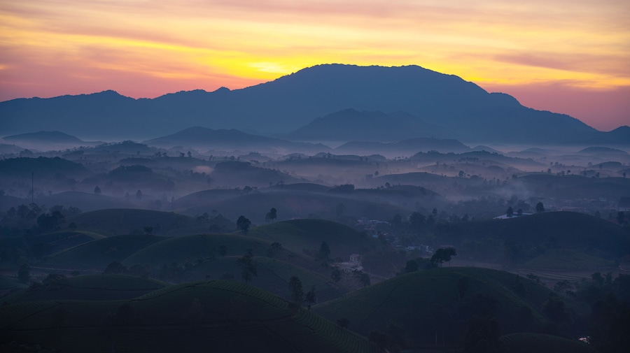 A mountainous landscape with rolling hills and a sunrise or sunset.