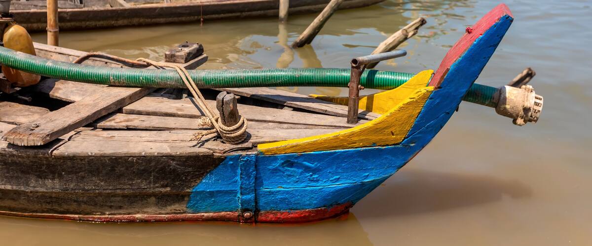 A wooden boat with a colorful painted bow, tied to a dock with a green hose.
