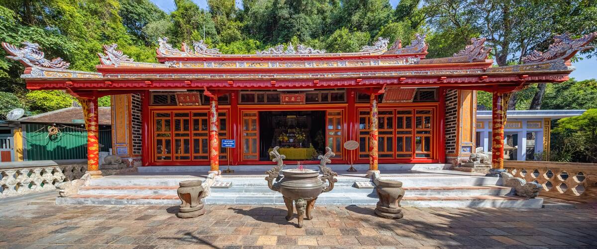 A traditional Chinese temple with ornate red and gold architecture, featuring dragon decorations on the roof and stone lion statues at the entrance.