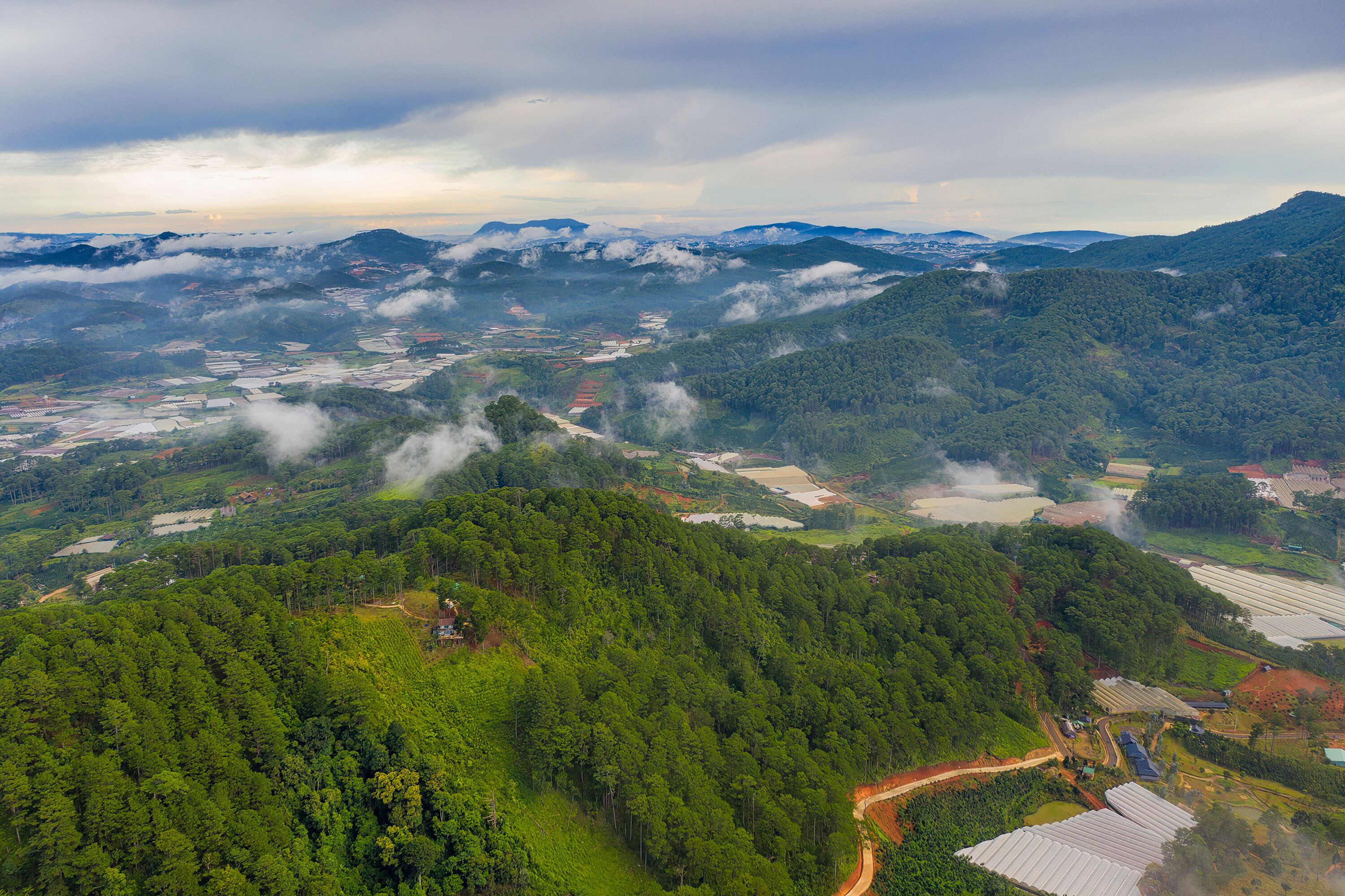 A mountainous landscape with dense forests, agricultural fields, and scattered buildings.
