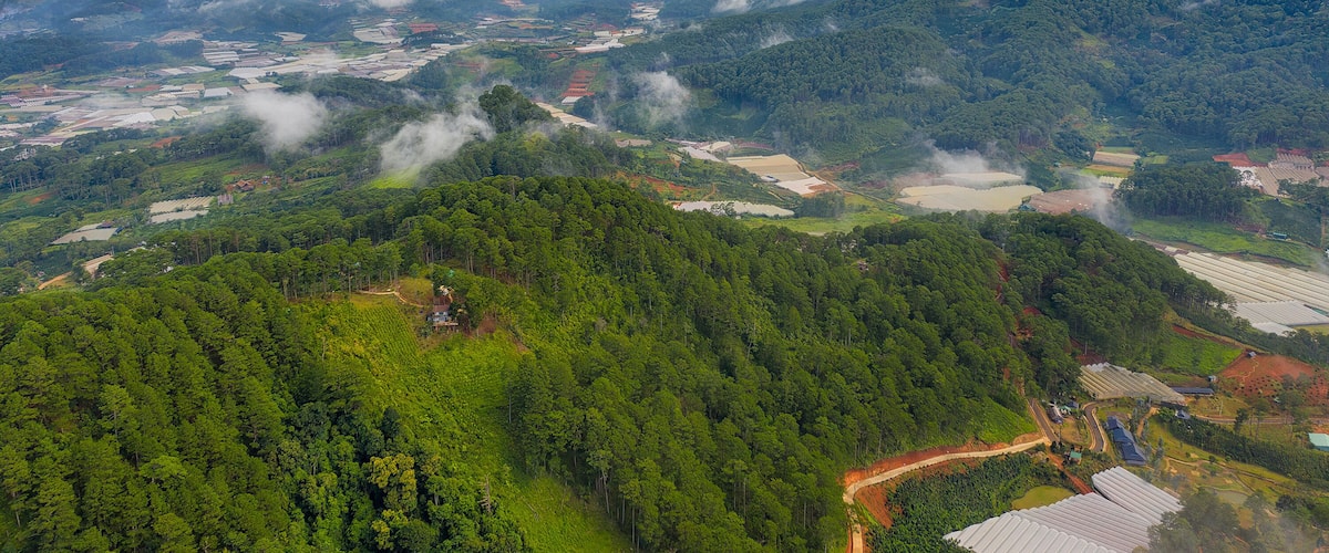 A mountainous landscape with dense forests, agricultural fields, and scattered buildings.