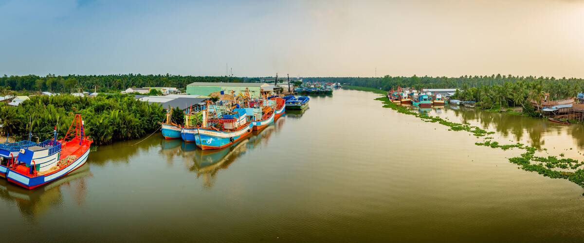 A river with several boats docked along the banks, surrounded by greenery and trees.