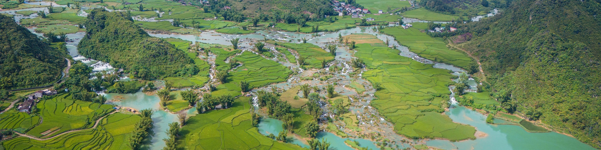 Un valle exuberante con campos de arroz en terrazas, un río serpenteante y un pequeño asentamiento.