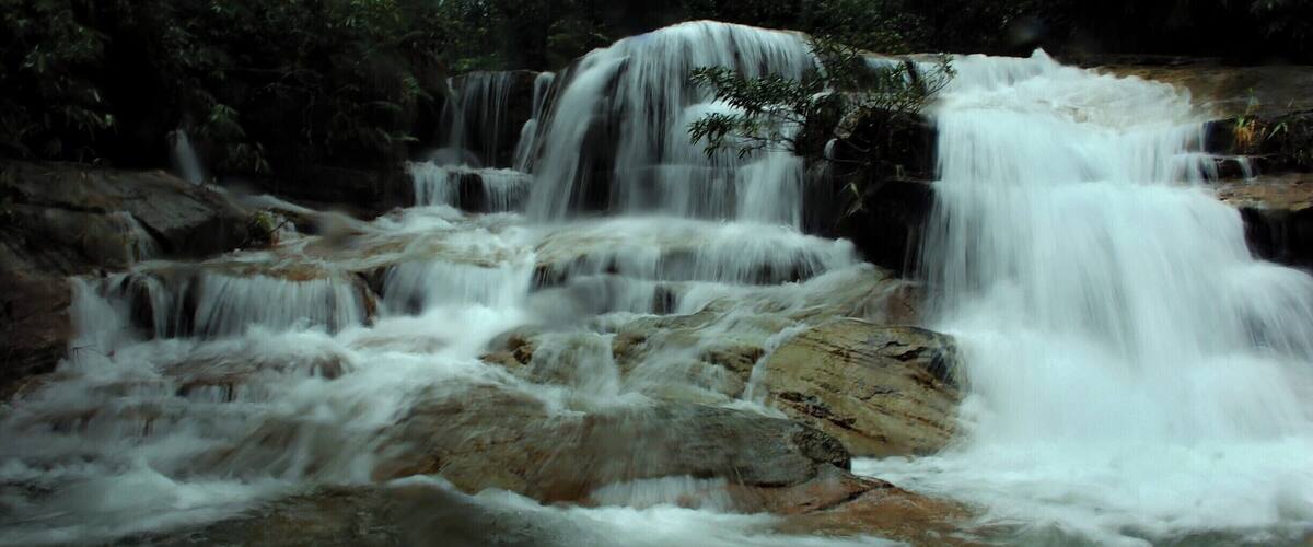 A multi-tiered waterfall with cascading water over rocks in a forested area.