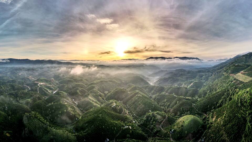 A mountainous landscape with a sunrise, terraced fields, and a winding road.