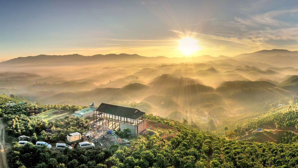 A mountainous landscape with a building surrounded by lush greenery and a clear sky.