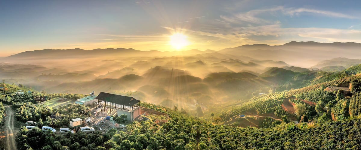 A mountainous landscape with a building surrounded by lush greenery and a clear sky.