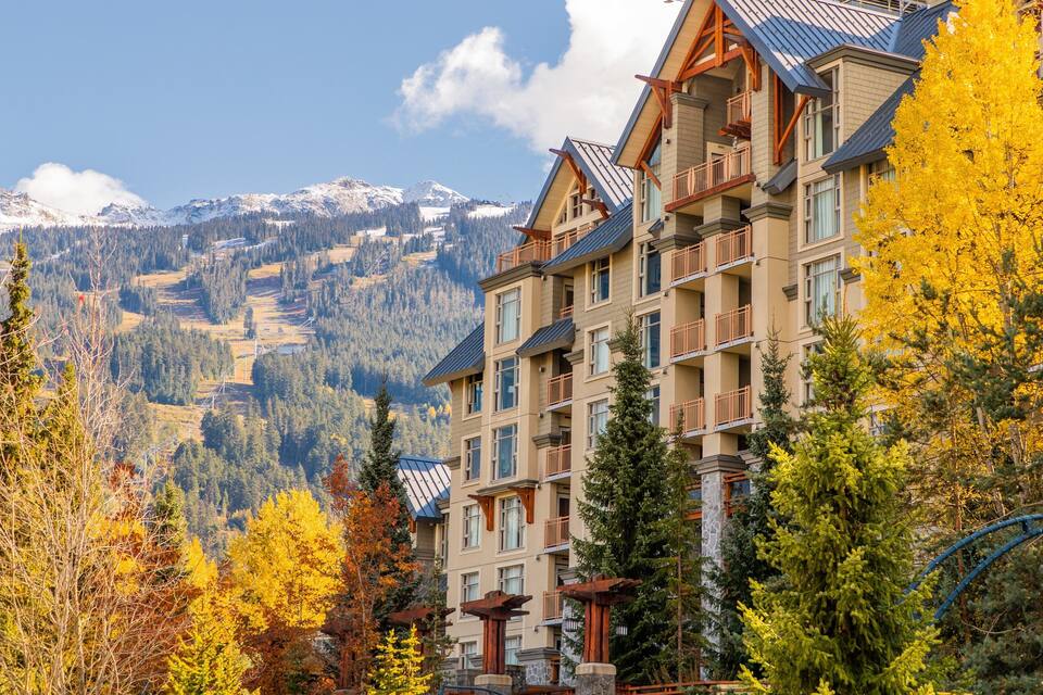 A mountain lodge with a ski lift, surrounded by autumn-colored trees and snow-capped mountains.