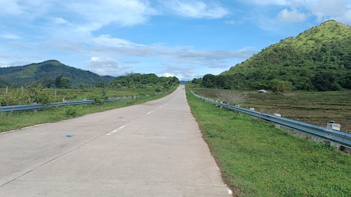 A paved road flanked by green hills and a clear sky.