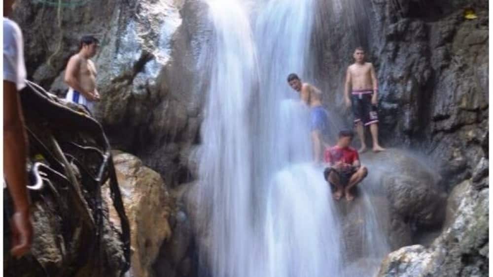 A waterfall cascading down rocky terrain with people standing and sitting around it.