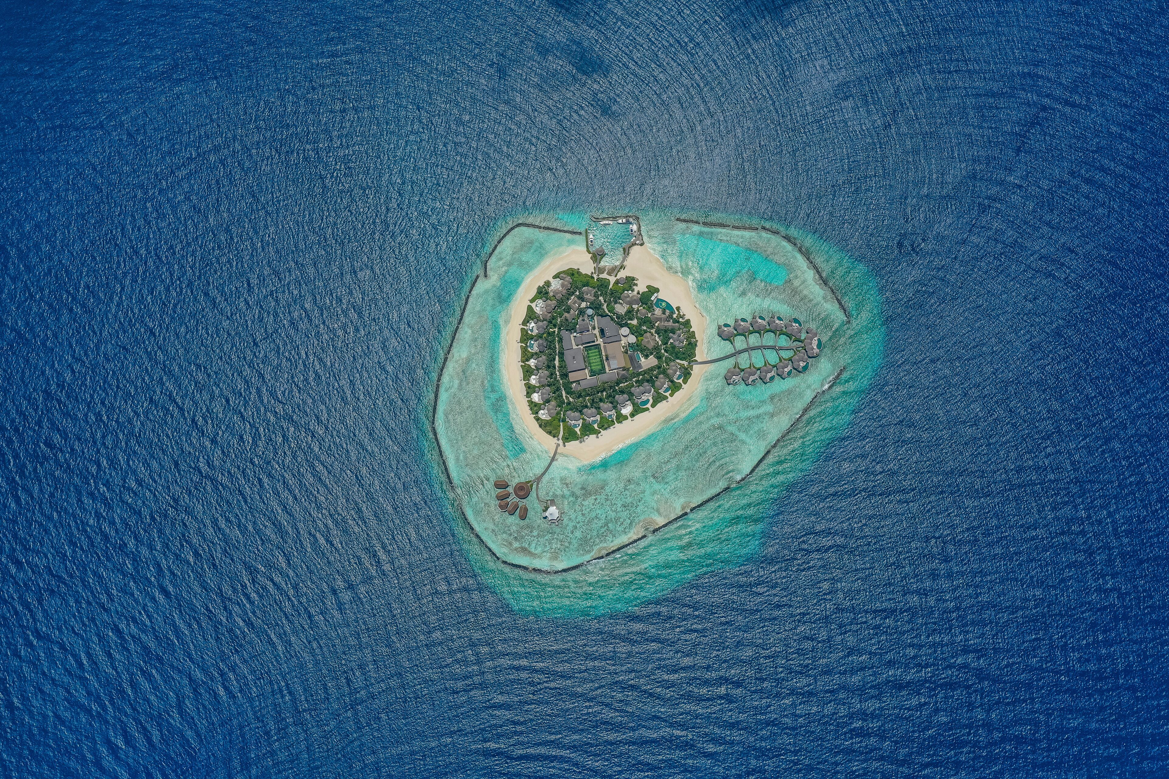 An aerial view of a small island with a central building surrounded by a beach and clear waters.