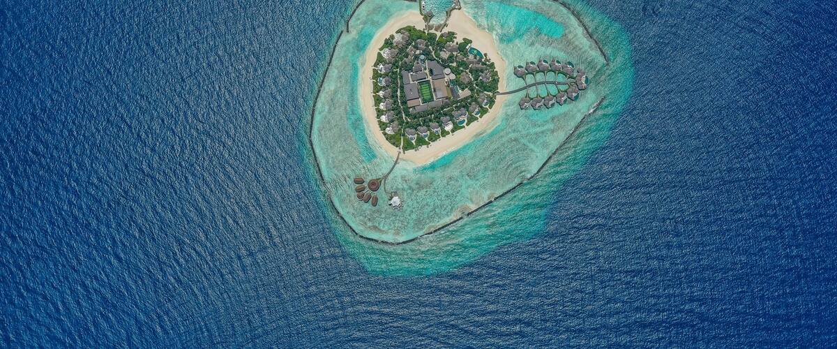 An aerial view of a small island with a central building surrounded by a beach and clear waters.