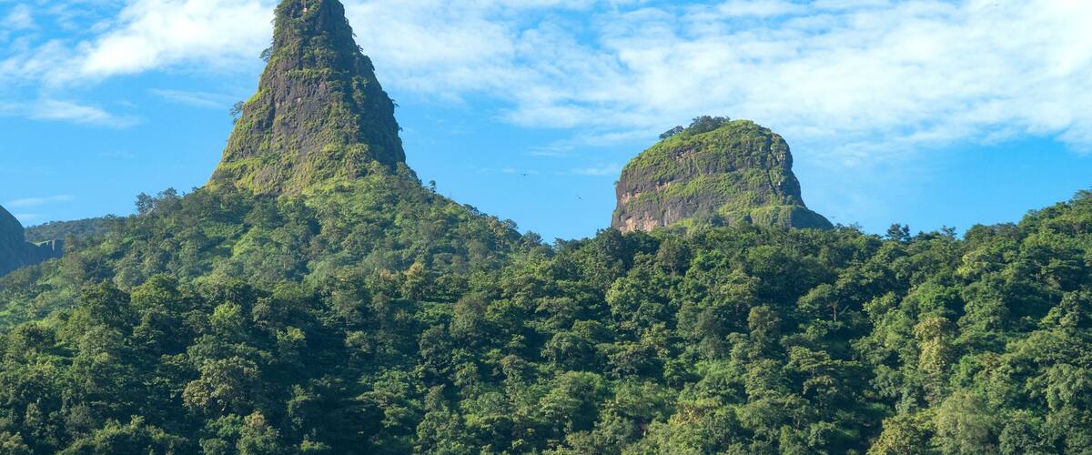 A mountainous landscape with lush green vegetation and two prominent peaks under a partly cloudy sky.