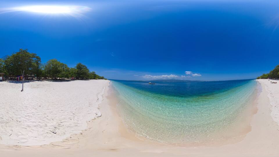 A beach with clear turquoise water, white sand, and trees in the background.