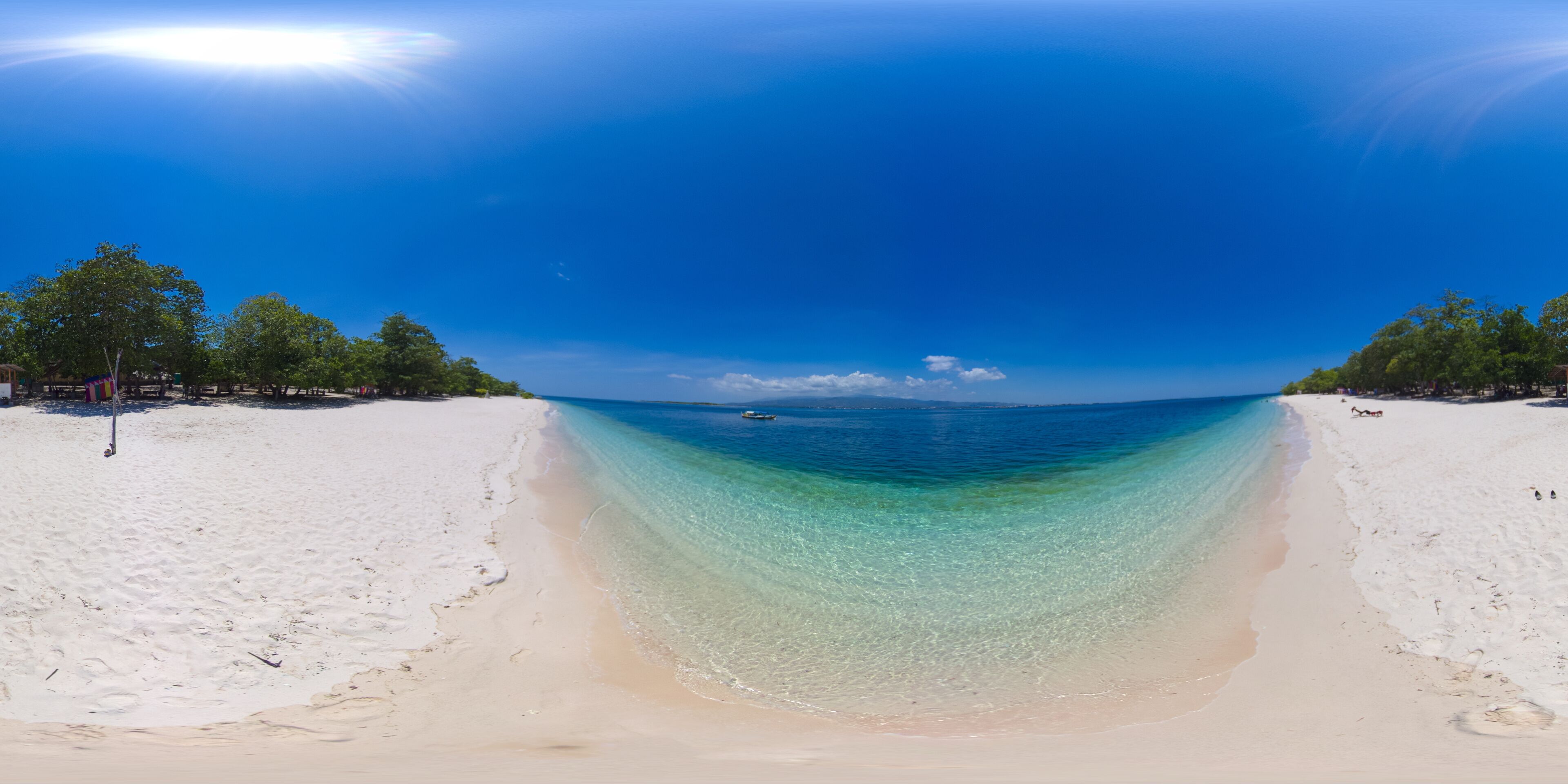 A beach with clear turquoise water, white sand, and trees in the background.