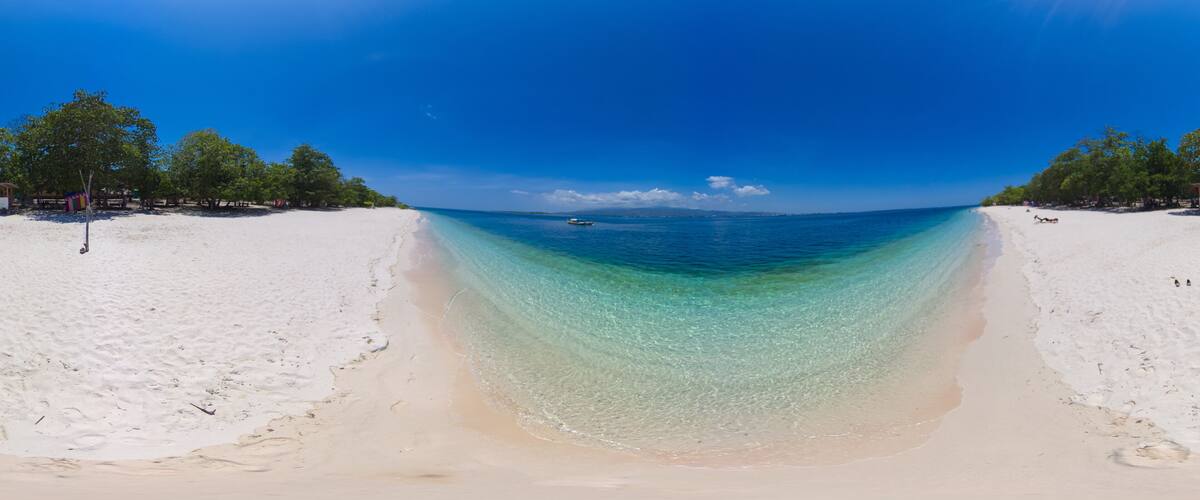 A beach with clear turquoise water, white sand, and trees in the background.