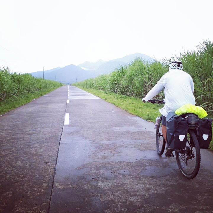 A cyclist on a wet road with mountains in the background.