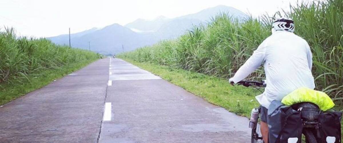 A cyclist on a wet road with mountains in the background.