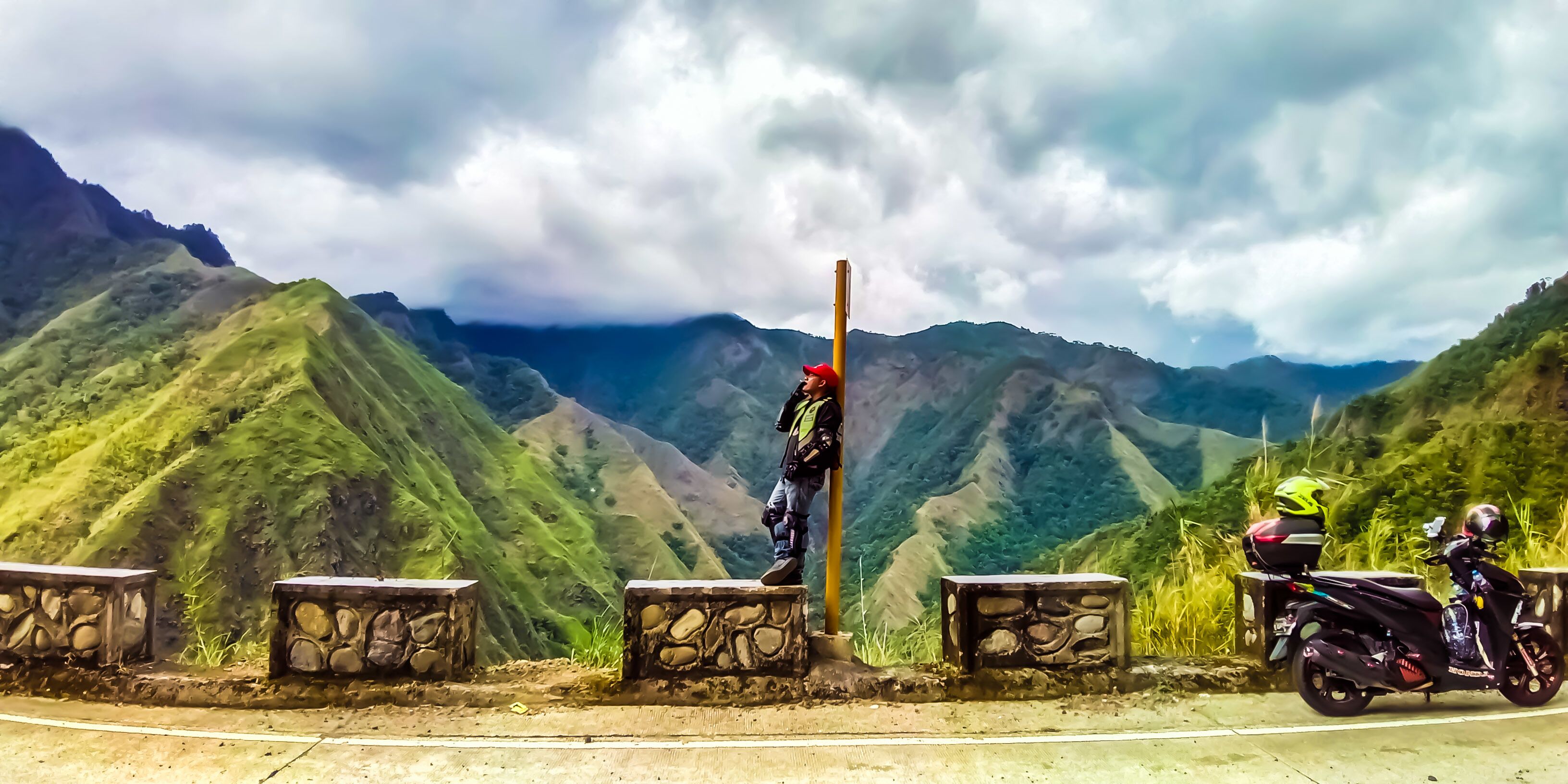 A person standing on a stone ledge with a mountain range in the background.