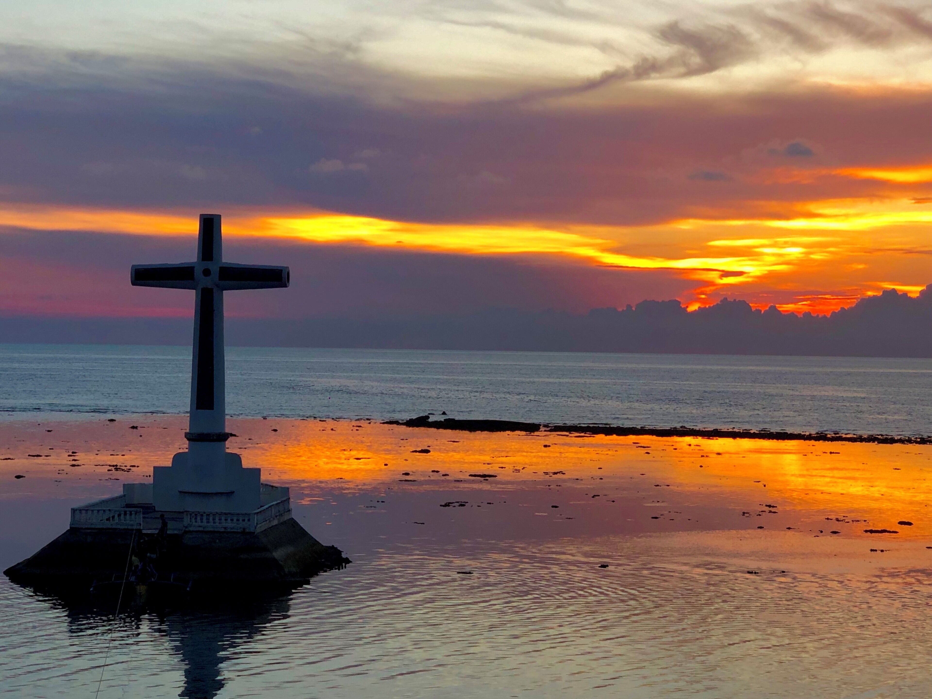 A cross on an island with a sunset in the background.