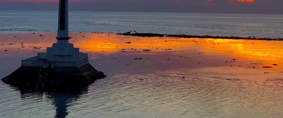 A cross on an island with a sunset in the background.