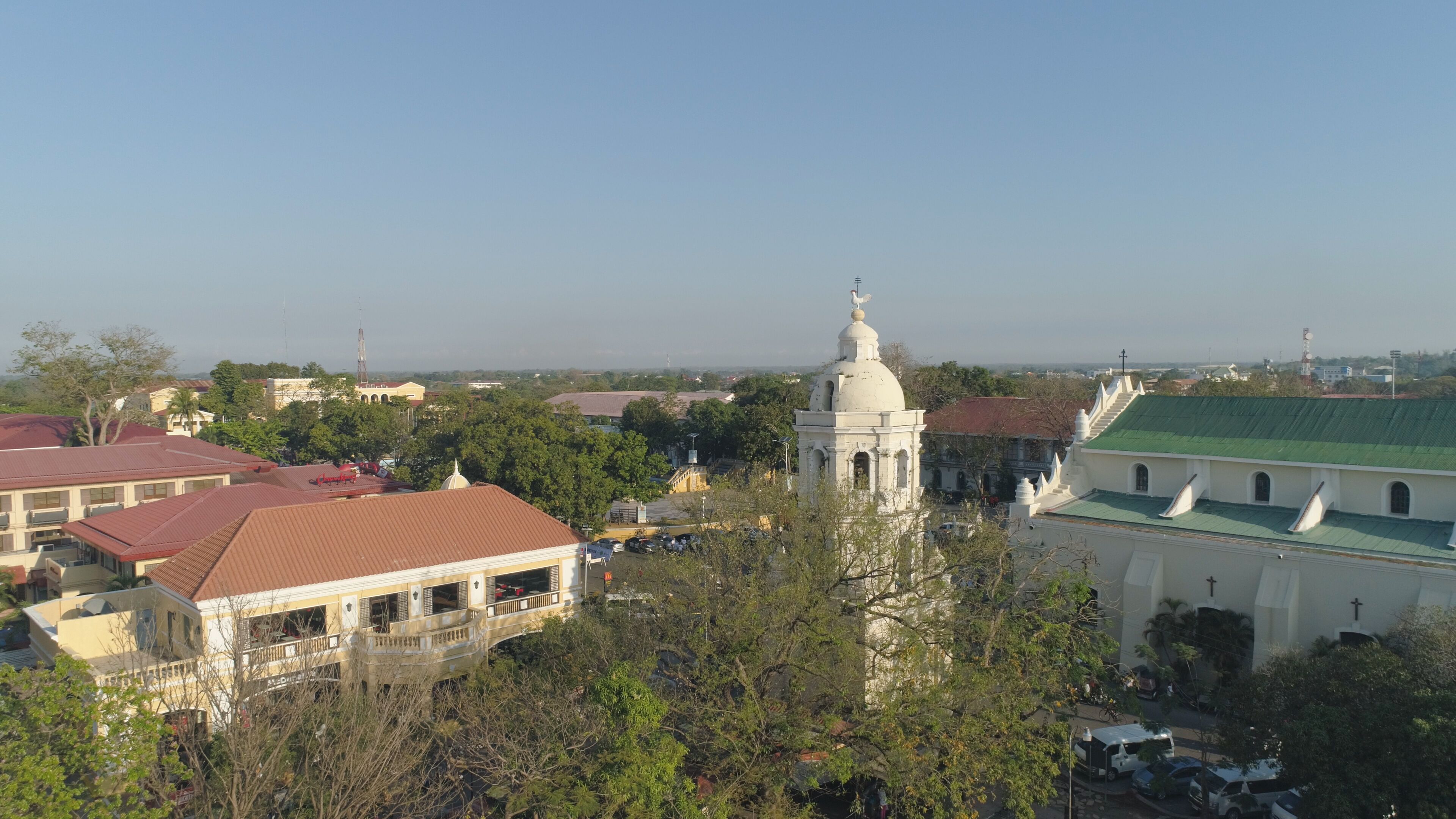 A cityscape with a prominent white church with a dome, surrounded by buildings with red roofs and a green-roofed structure.
