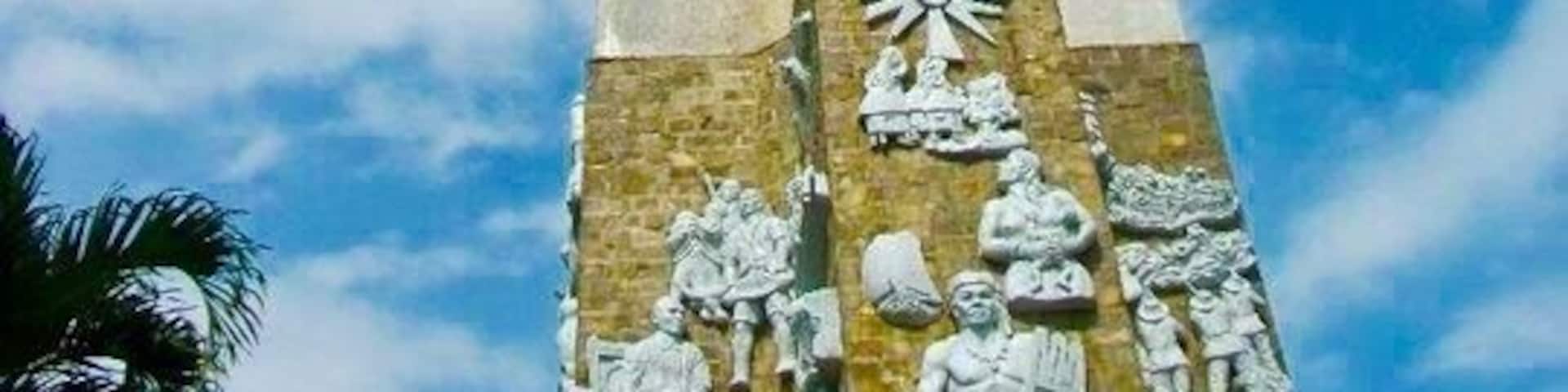 A tall monument with a cross at the top and relief sculptures at the base.