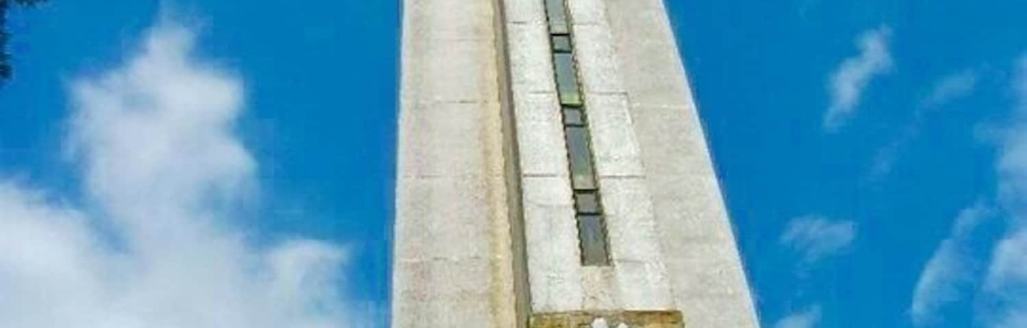 Um monumento alto com uma cruz no topo e esculturas em baixo-relevo na base.