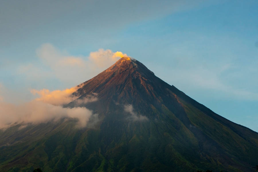 A mountain with a peak, clouds, and a clear sky.