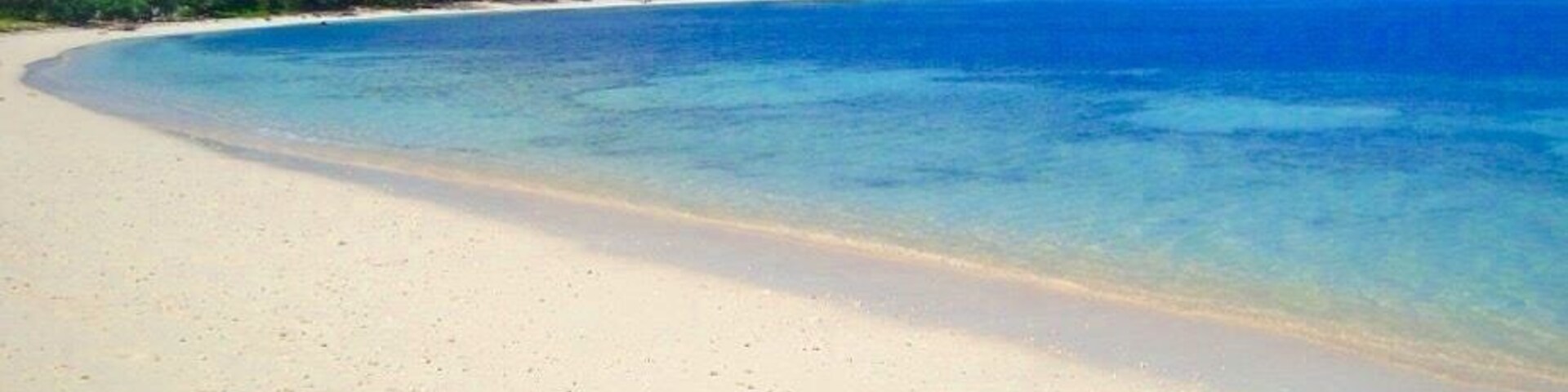 Una playa arenosa con aguas azules cristalinas y colinas verdes al fondo.