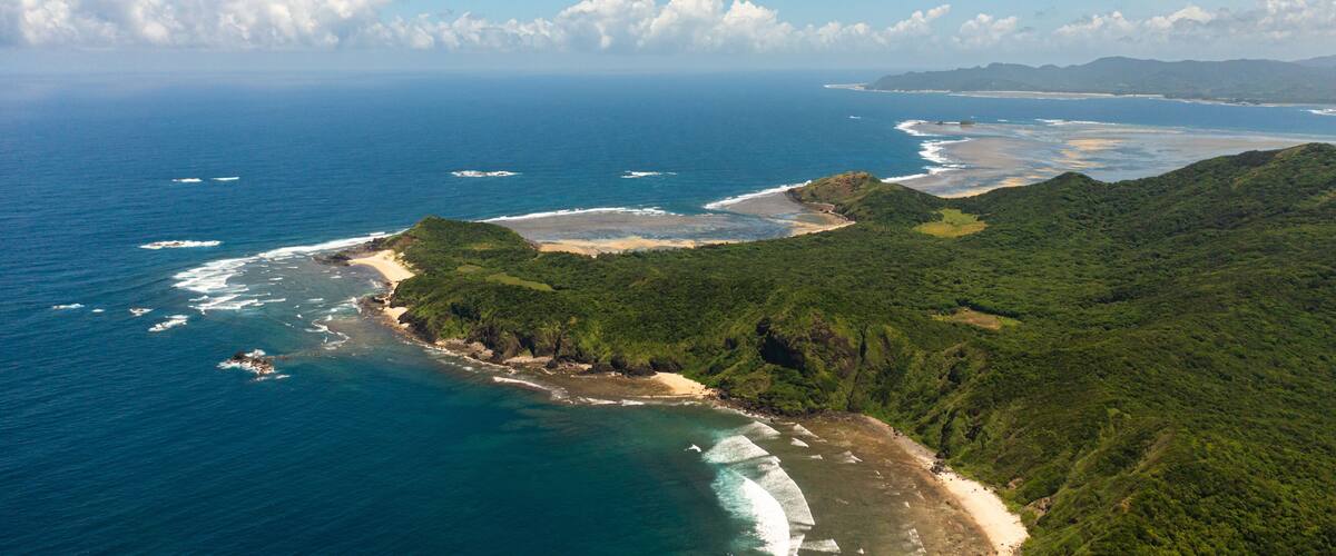 A coastal landscape with a beach, ocean, and lush green hills.
