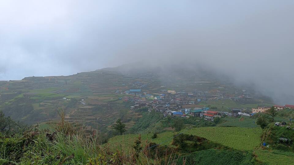 A misty village nestled in terraced fields on a hillside.