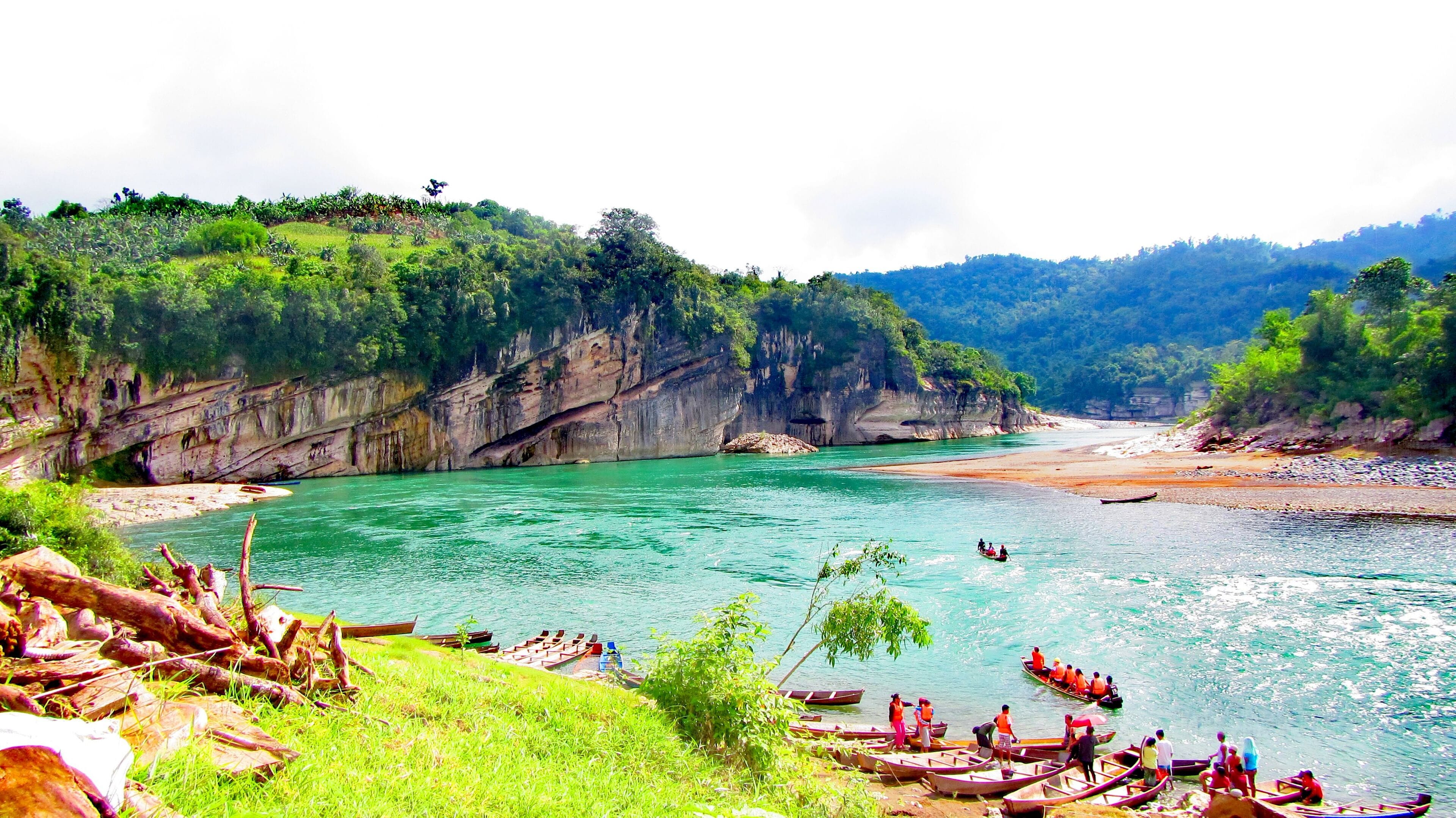 A river with boats, rocky cliffs, and lush greenery.