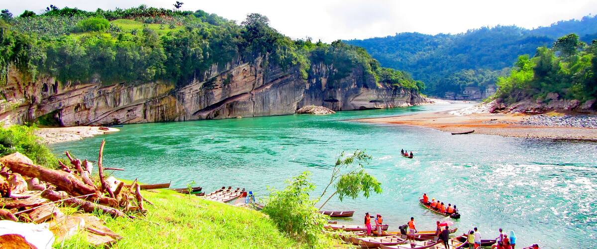 A river with boats, rocky cliffs, and lush greenery.