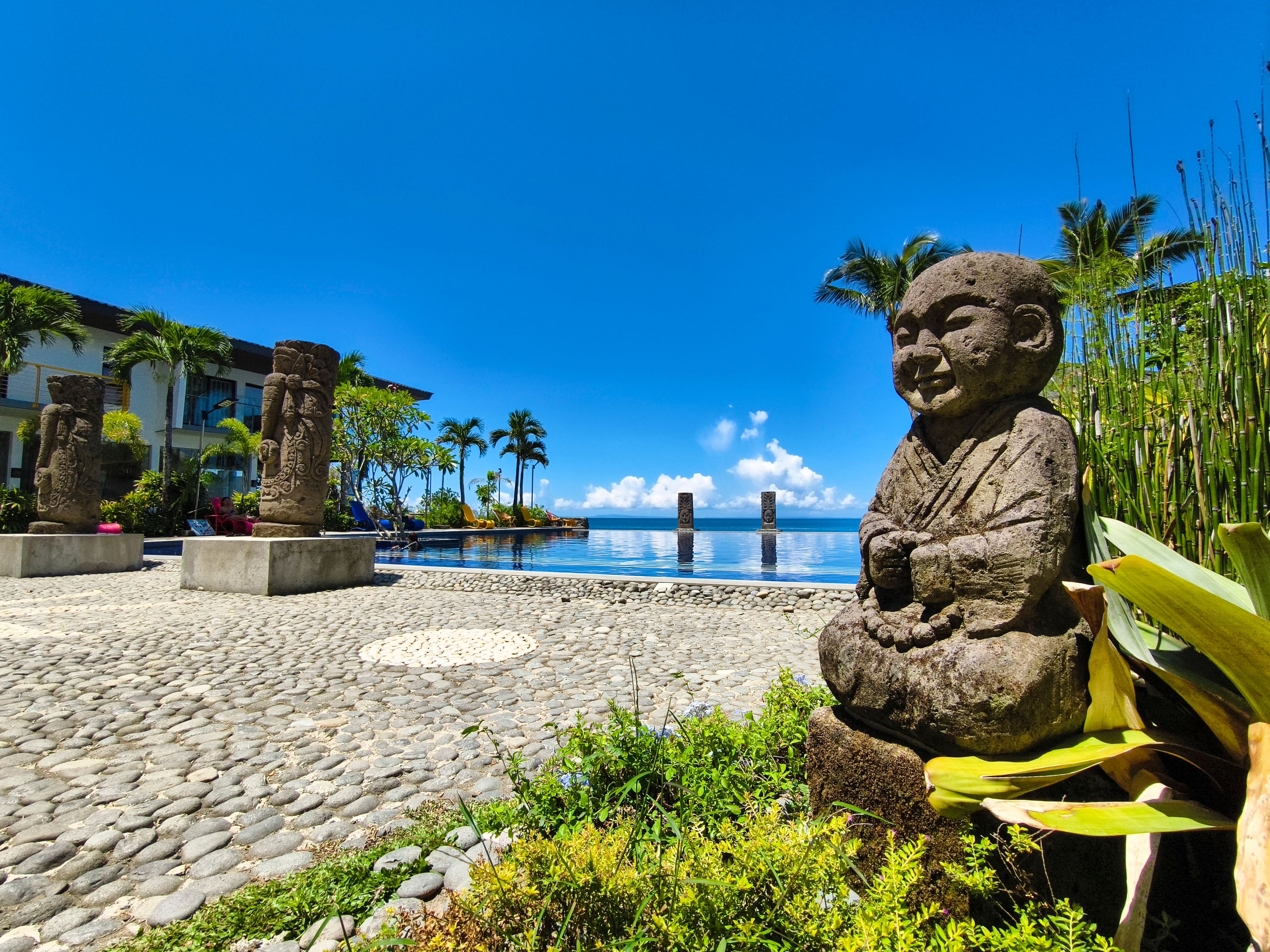 A stone Buddha statue, a pool, and a tropical resort setting.